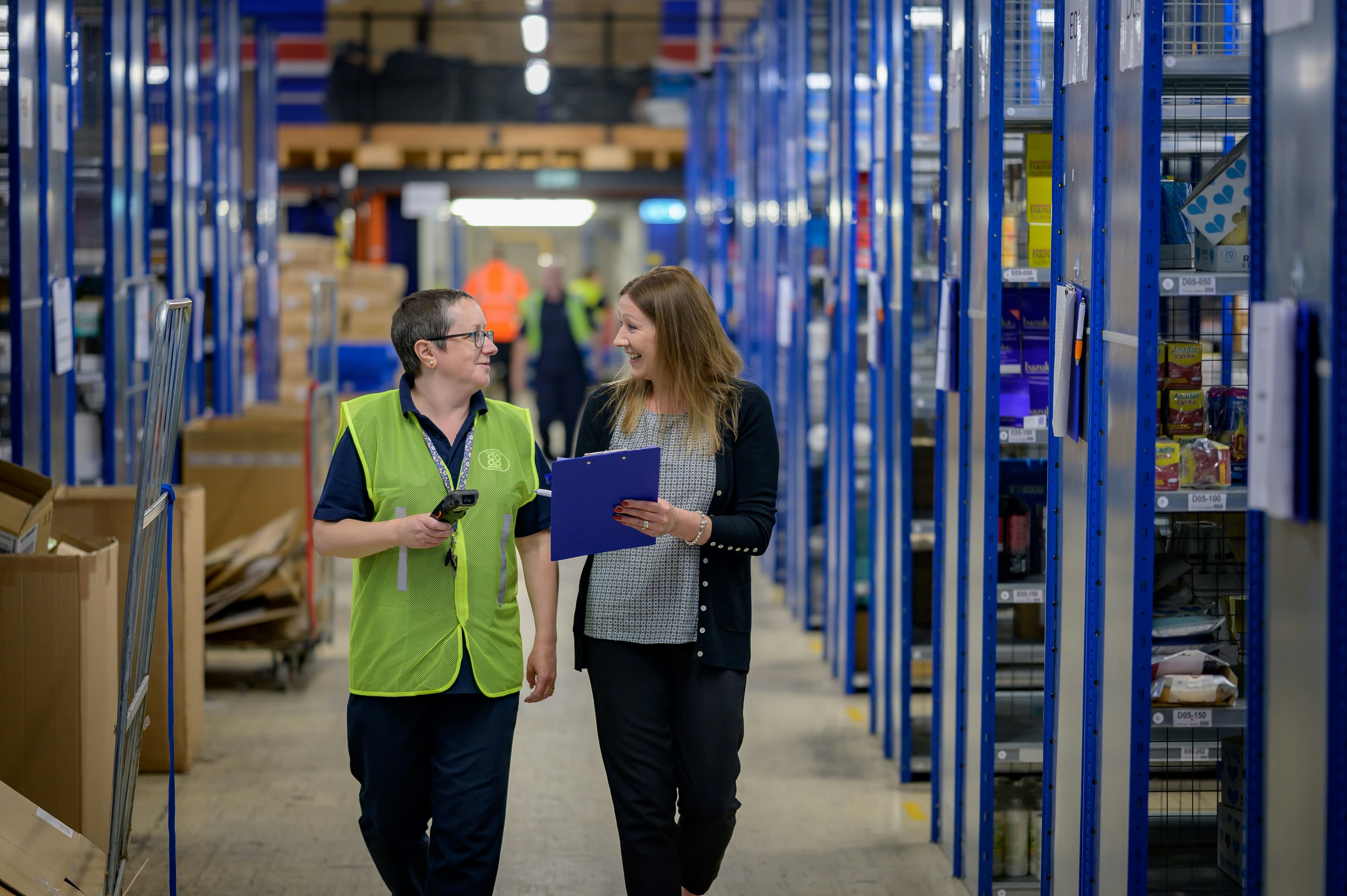 Two colleagues walking and talking together in a warehouse aisle